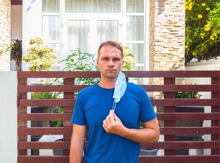 Portrait of guy with a medical mask. Outside walking in the garden near modern summer house. He wants to breathe, wait for the end of quarantine Covid19 isolation and beginning of normal life againの写真素材