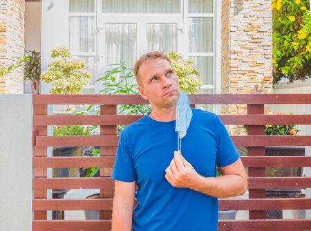 Portrait of guy with a medical mask. Outside walking in the garden near modern summer house. He wants to breathe, wait for the end of quarantine Covid19 isolation and beginning of normal life againの写真素材
