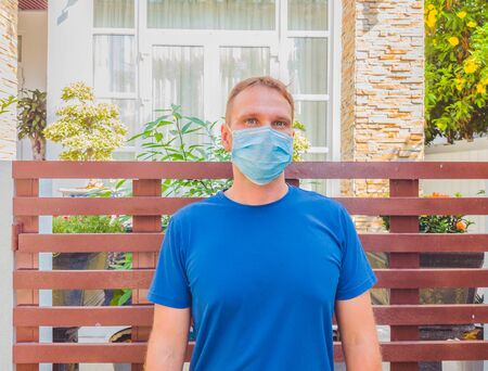 Portrait of guy with a medical mask. Outside walking in the garden near modern summer house. He wants to breathe, wait for the end of quarantine Covid19 isolation and beginning of normal life againの写真素材