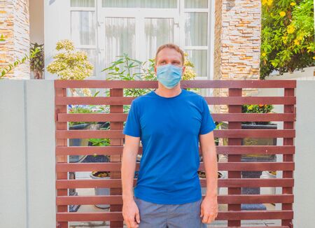 Portrait of guy with a medical mask. Outside walking in the garden near modern summer house. He wants to breathe, wait for the end of quarantine Covid19 isolation and beginning of normal life againの写真素材