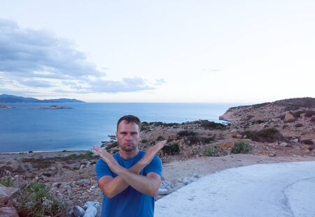 Serious man standing with crossed hands on a sunset mountain rock and sea background. Stop vacation, travel because of coronavirus or be careful in wild nature conceptの写真素材