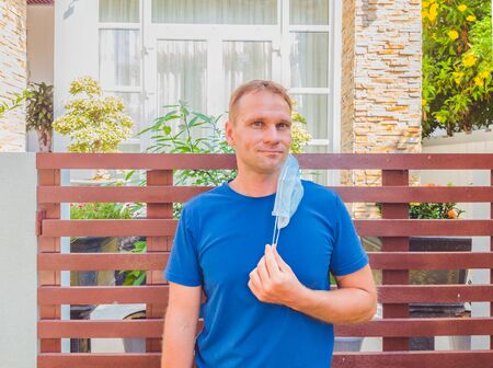 Portrait of guy with a medical mask. Outside walking in the garden near modern summer house. He wants to breathe, wait for the end of quarantine Covid19 isolation and beginning of normal life againの写真素材