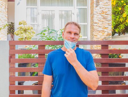 Portrait of guy with a medical mask. Outside walking in the garden near modern summer house. He wants to breathe, wait for the end of quarantine Covid19 isolation and beginning of normal life againの写真素材