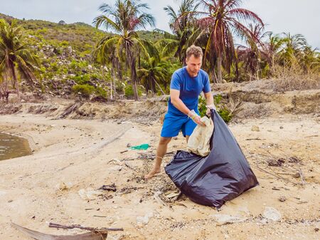Man in gloves pick up plastic bags that pollute sea. Problem of spilled rubbish trash garbage on the beach sand caused by man-made pollution and environmental, campaign to clean volunteer in conceptの写真素材