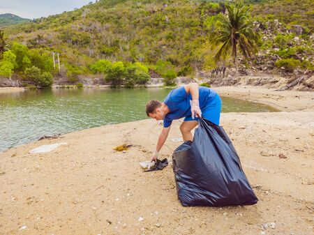 Man in gloves pick up plastic bags that pollute sea. Problem of spilled rubbish trash garbage on the beach sand caused by man-made pollution and environmental, campaign to clean volunteer in conceptの写真素材