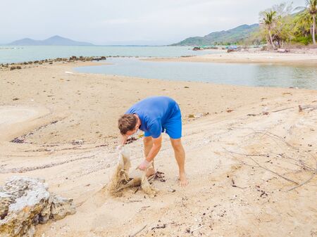 Man in gloves pick up plastic bags that pollute sea. Problem of spilled rubbish trash garbage on the beach sand caused by man-made pollution and environmental, campaign to clean volunteer in conceptの写真素材