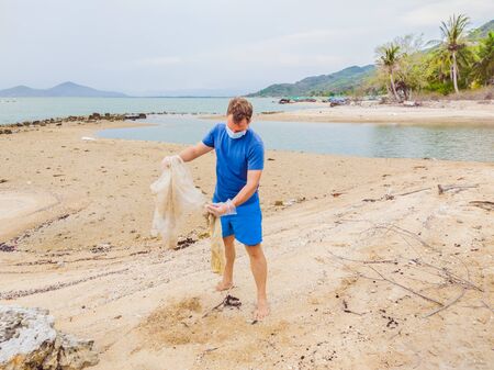 Man in gloves pick up plastic bags that pollute sea. Problem of spilled rubbish trash garbage on the beach sand caused by man-made pollution and environmental, campaign to clean volunteer in conceptの写真素材