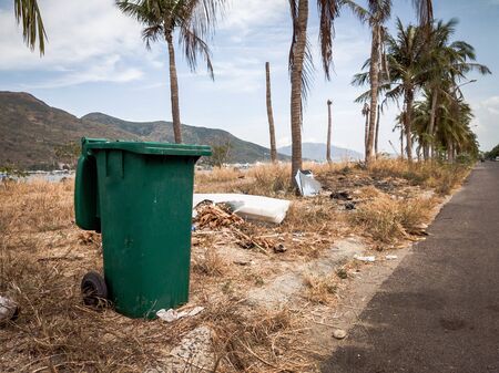 Opened big empty green plastic trash garbage bin in modern comfortable village near sea and palms. Public trash on the side of the road. Infectious control, garbage disposal, disposal of waste conceptの写真素材