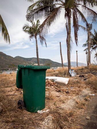 Opened big empty green plastic trash garbage bin in modern comfortable village near sea and palms. Infectious control, garbage disposal, disposal of waste concept. Stories vertical formatの写真素材