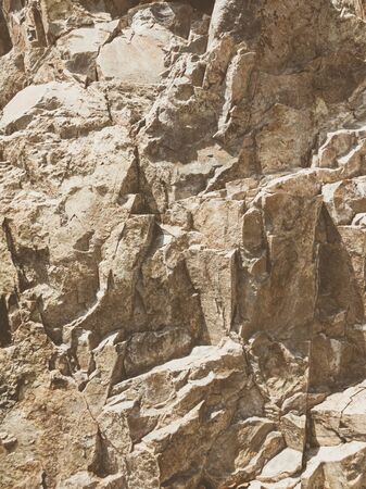 Natural background. Closeup edged shabby cliff cracks. Gray-brown stone rock texture of mountains. Vintage and faded matt style colour in tinted photo. Concept of geolog, mountaineering or hard work.の写真素材