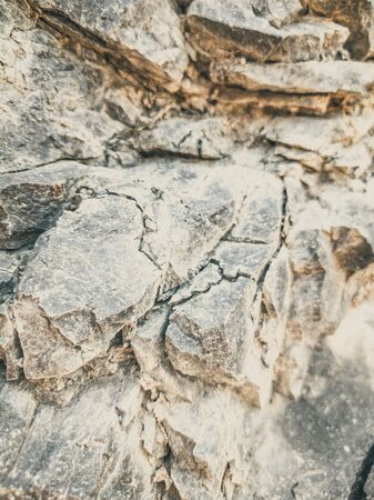 Natural background. Closeup edged shabby cliff cracks. Gray-brown stone rock texture of mountains. Vintage and faded matt style colour in tinted photo. Concept of geolog, mountaineering or hard workの写真素材