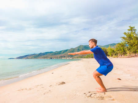Young beautiful man doing sport performing workouts exercises near sea in the morning during quarantine. Active life without surgical sterilizing face mask protectionの写真素材