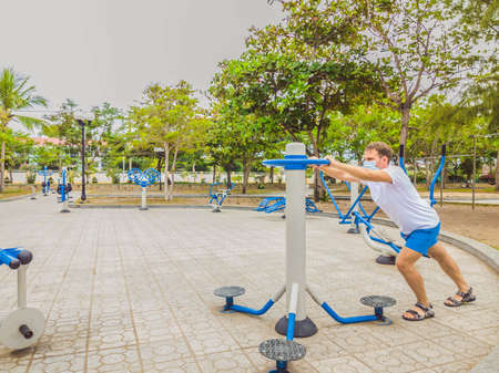 Man doing physical exercises, push ups, strength exercises, leans in empty outdoor public city park metal gym wearing mask alone for Covid19 prevention. Healthy lifestyle in quarantine and coronavirusの写真素材