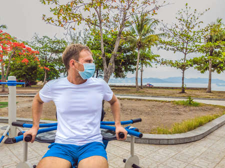 Man doing physical exercises, push ups, strength exercises, leans in empty outdoor public city park metal gym wearing mask alone for Covid19 prevention. Healthy lifestyle in quarantine and coronavirusの写真素材