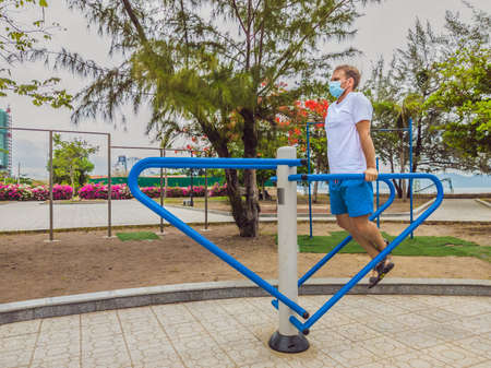 Man doing physical exercises, push ups, strength exercises, leans in empty outdoor public city park metal gym wearing mask alone for Covid19 prevention. Healthy lifestyle in quarantine and coronavirusの写真素材