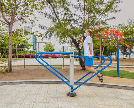 Man doing physical exercises, push ups, strength exercises, leans in empty outdoor public city park metal gym wearing mask alone for Covid19 prevention. Healthy lifestyle in quarantine and coronavirusの写真素材