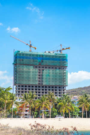 Modern big residential or office high rise building under construction against blue sky with tower crane near sea beach palm. Real estate, construction business, buying investing in apartments abroadの写真素材