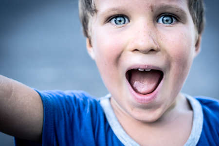 Portrait of a funny happy mischievous cheerful cute blond blue eyed boy making freckles dirty face while playing, laughing. Nursery, happy childhood, education, family relationship conceptの写真素材