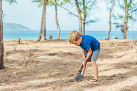 Camping people outdoor lifestyle tourists, summer forest near lazur sea. Blond boy play study survival techniques, practice methods to dig the earth with a shovel. Natural children educationの写真素材