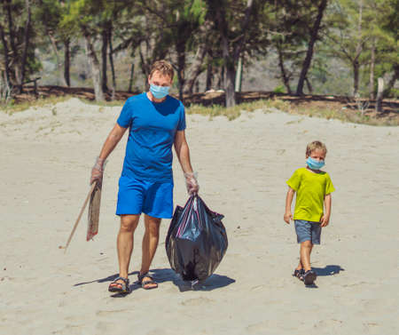 Volunteers with blue face mask forest sand beach. Son going, father hold black bag with picked up...