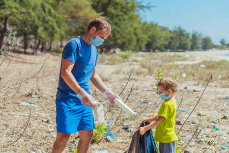 Volunteer blue face mask forest sand beach. Son helps father hold black bag for pick up garbage. Problem spilled rubbish trash planet pollution environmental protection. Natural children educationの写真素材