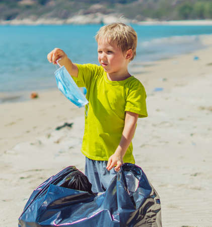 Volunteers beach sand lazur sea. Boy pick up garbage into black bag. Son refuse to wear blue face...