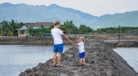 Father son walk near mountain lake, look point at each other, winking playing. Happy childhood. Home natural child education, fathers day, dad responsibilities, influence on son worldview formationの写真素材