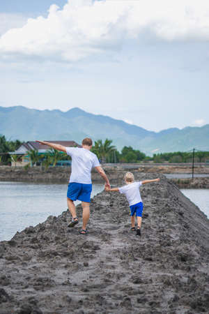 Father son walk near mountain lake, play show outstretched hands like airplane. Happy childhood. Home natural child education, fathers day, dad responsibilities, influence on son worldview formationの写真素材