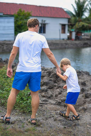 Father take care about son while walking near mountain lake holds leads by the hand. Happy childhood. Home natural education, fathers day, dad responsibilities, influence on son worldview formationの写真素材
