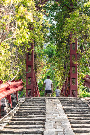 Bottom view of gray brick stone stair steps leading to red iron suspension pedestrian bridge in...