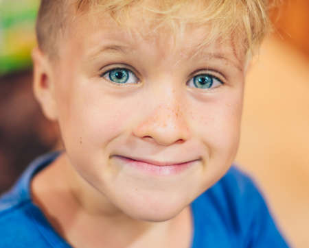 Close up portrait cute smiling blue eyed freckled blond boy pronounced artistic facial expressions, gestures, intriguing cunning funny mischievous. Happy childhood, children behaviour problems conceptの写真素材