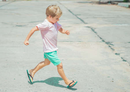 Smiling freckled blond boy autistic facial expressions, run marching hands gestures, mischievous in good mood, summer flip flops sandal. Funny photo, happiness lifestyle simple joys childhood childrenの写真素材
