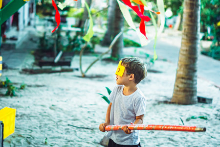 Side view little kid boy wearing lego style yellow face mask gesturing preparing to hit pinata with...