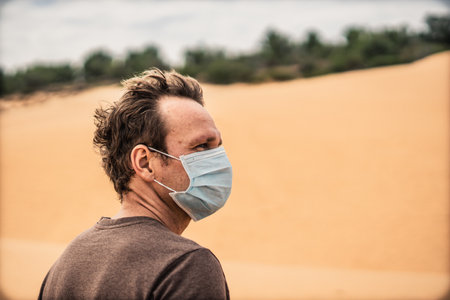 Side portrait young man wear protective mask, face expression emotion look far away dune. Concept COVID stress syndrome, mental health, fear of danger contamination, adverse socio economic consequenceの写真素材
