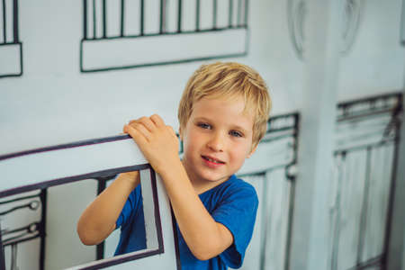 Portrait smile blue eyed freckled blond boy, hide behind chair, micro facial expression hand gesture. Funny mischievous mood. Happy childhood, child behaviour education psychology relationship conceptの写真素材