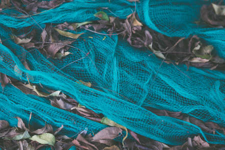 Close-up view of green nylon multi colorful bright fish nets in a pile of dry leaves in fishing village. Still life background pattern. Hobby fishing concept. Copy space. Autumn mood collectionの写真素材