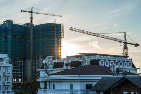 Modern big multi-storey residential or office high rise building under construction, sunrise sky background, tower cranes. Real estate business, buying investing in apartments abroad, mortgageの写真素材
