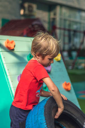 VERTICAL Boy play practice balance motor coordination training. Jump go step carry car tires. Concept outdoor fun, open air sport game classes, obstacle course for child improve efficiency raising sonの写真素材