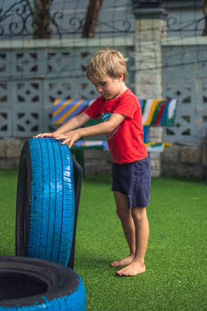 VERTICAL Boy play practice balance motor coordination training. Jump go step carry car tires. Concept outdoor fun, open air sport game classes, obstacle course for child improve efficiency raising sonの写真素材