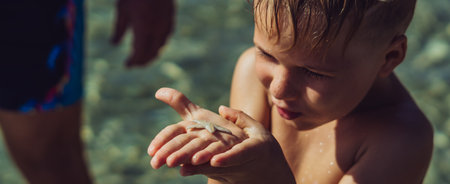 BANNER Copy space. Close side lifestyle portrait boy carefully thoughtful surprise facial expression look at white little starfish on palm. Day sun sea. Childhood learn new interest kid tourism happyの写真素材
