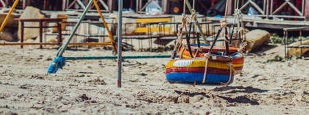BANNER Hang rope swing old tires paint bright multicolor orange blue yellow red metal frame veranda roof. Nature sand beach background. Day sun summer. Child kindergarten joy sandbox playgroundの写真素材