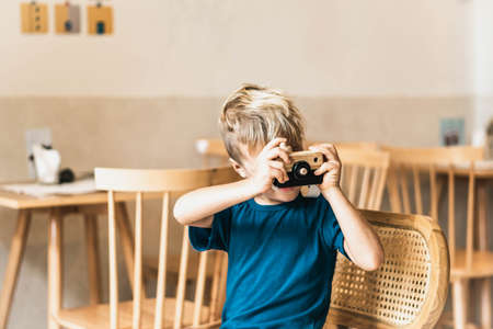 Cute happy smile little boy play handmade wooden photo camera, hold toy in hands. Artistic craft...
