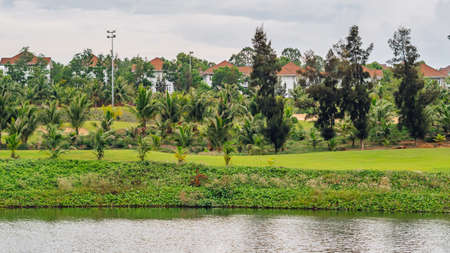 Beautiful nature landscape wallpaper background. Bright green colours summer day morning time. Tropical Modern cottage villas orange roofs village near pond water palm trees bushes. Luxuryの写真素材