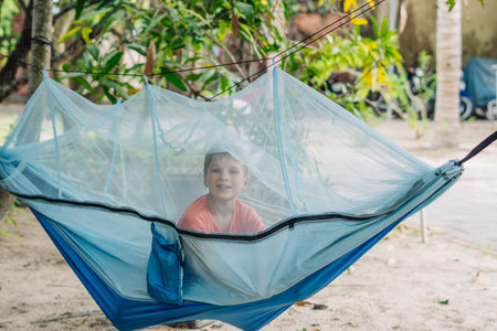 Smile child boy lie rest hammock with mosquito net. Happy childhood daydream. Look at from, laughing, portraitの写真素材