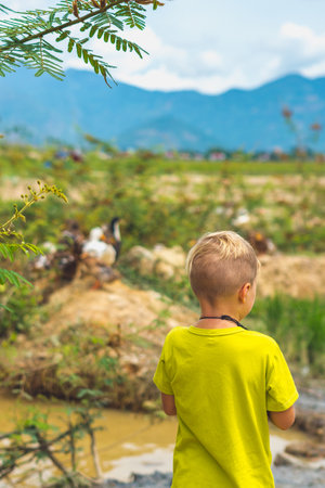 A boy in a yellow shirt stands in front of a mountain landscapeの写真素材
