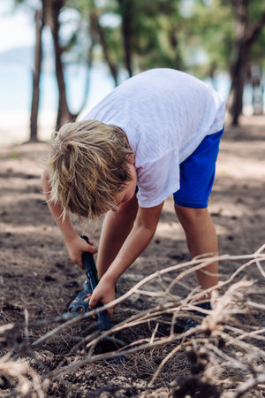 Cute boy digging soil in forest near sea beach. Family natural education skills. Travelling together. Learning camping organizing bonfireの写真素材