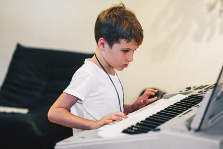 Young boy Portrait sitting at digital piano Playing keyboard focused kid activity indoors press on Key learning to play music room Hobbyの写真素材