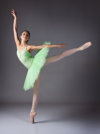 Beautiful female ballet dancer on a grey background. Ballerina is wearing a green tutu and pointe shoes.の写真素材