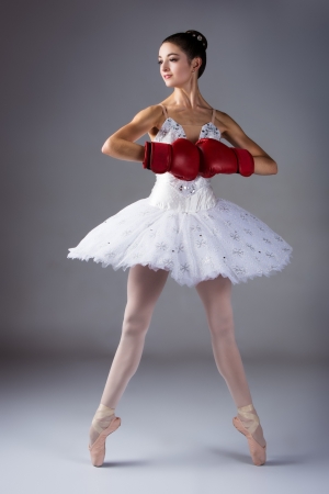 Beautiful female ballet dancer on a grey background  Ballerina is wearing a white tutu, pointe shoes and red boxing gloves の写真素材