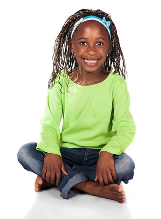 Adorable small african child with braids wearing a bright green shirt and blue jeans. The girl is sitting and smiling at the camera.の写真素材